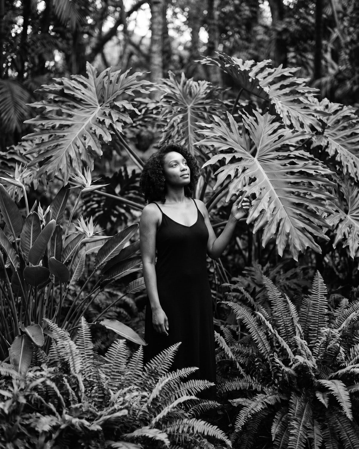 Black-and-white portrait of a woman in an off-shoulder dress among large tropical botanicals.