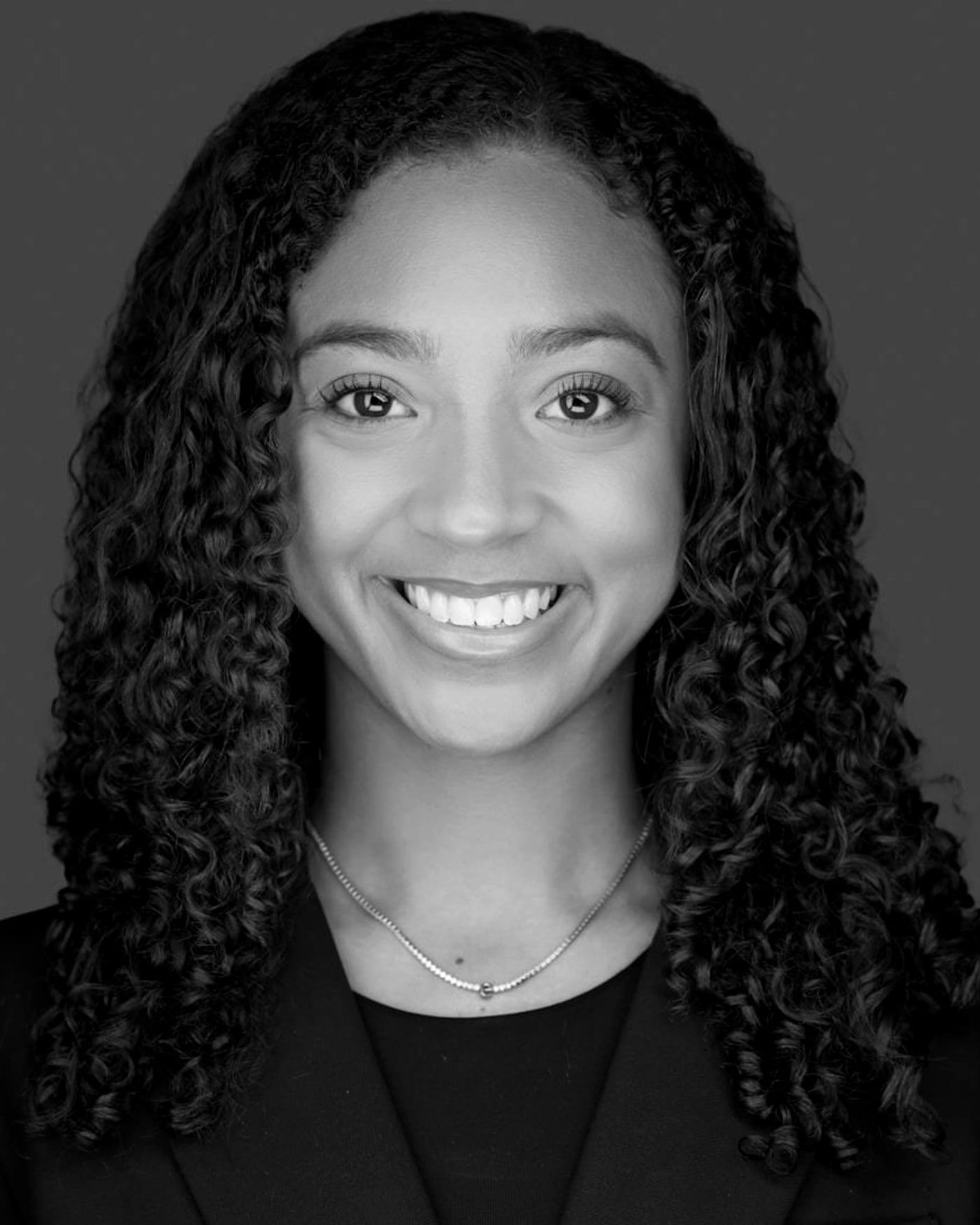 Black-and-white fine-art portrait of a woman with curls against a soft gray background.